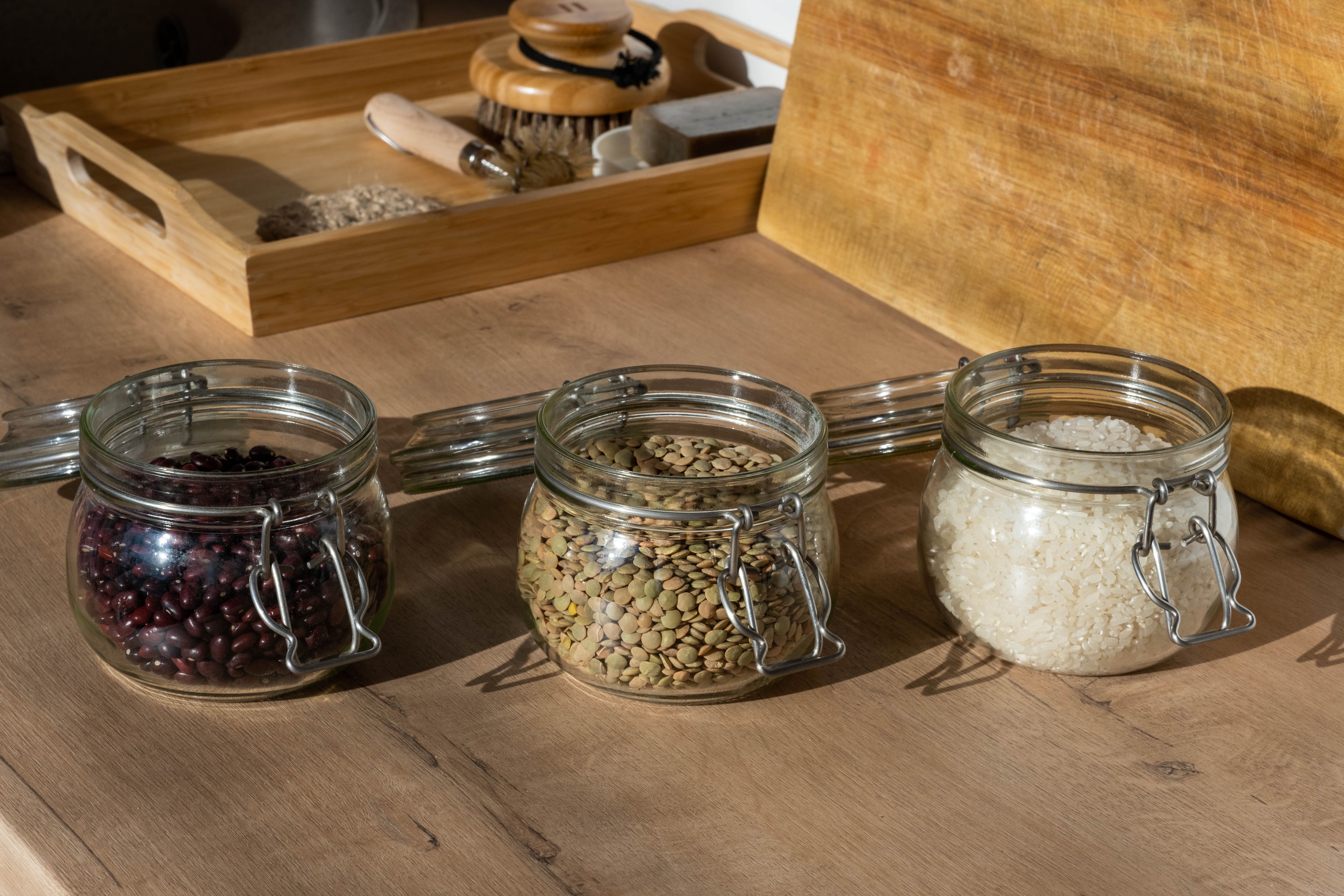 Clear clip-top jars of dried beans, lentils and rice on a wooden counter
